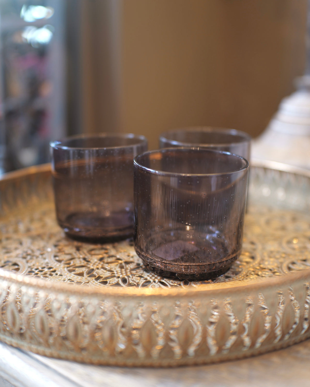 Three smoked glass tumblers on an ornate metal tray.