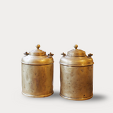 Two brass canisters with lids on a light gray background