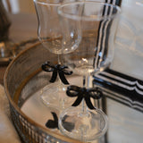 Two clear stemmed drinking glasses with black ribbon bows tied near the stems, displayed on a mirrored tray in an indoor setting.