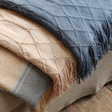 A stack of three textured woven throw blankets in navy blue, beige, and tan, draped over a sofa in a cozy indoor setting.