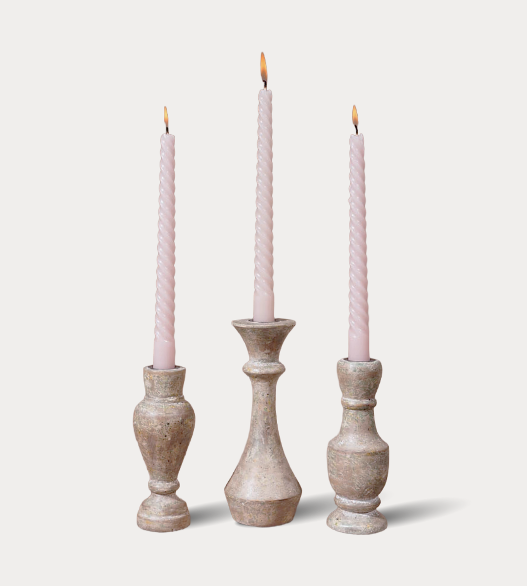 Three candlesticks with pink candles on a light gray background