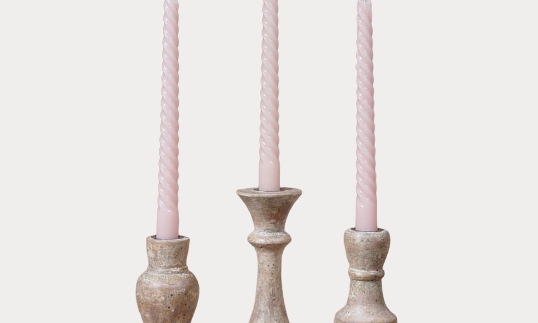 Three candlesticks with pink candles on a light gray background