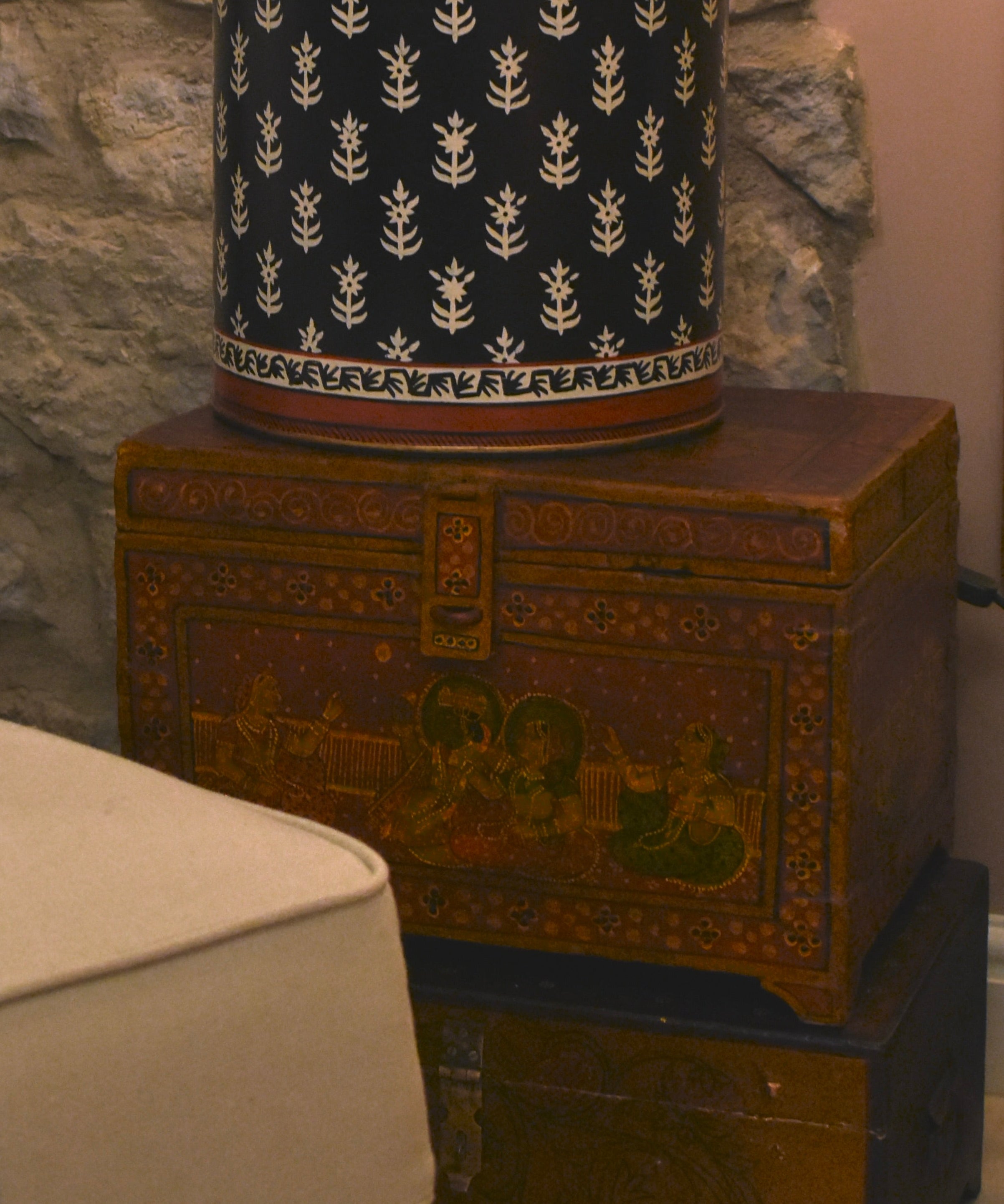 Decorative lamp on a wooden chest against a stone wall with a chair in the foreground.