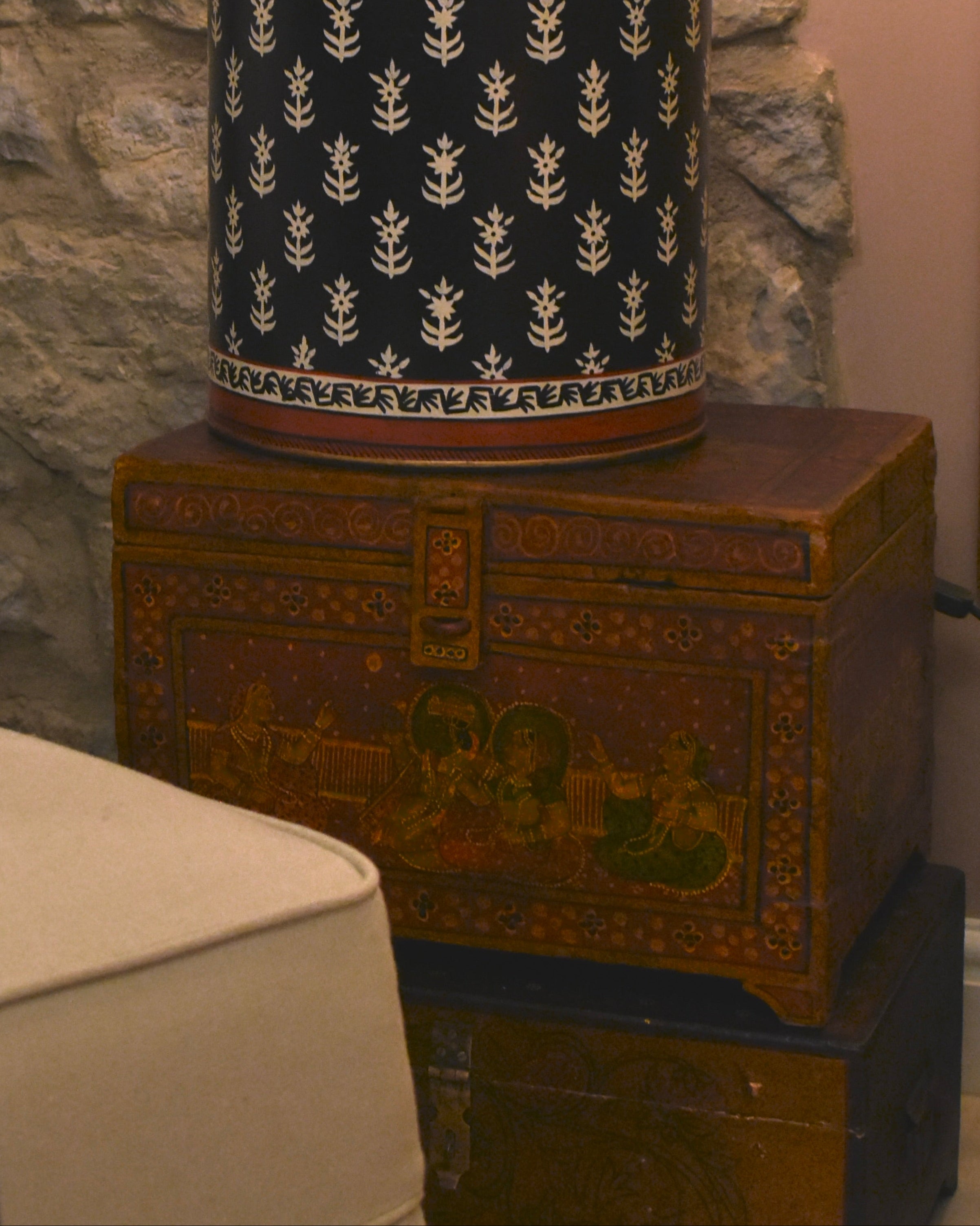 Decorative lamp on a wooden chest against a stone wall with a chair in the foreground.