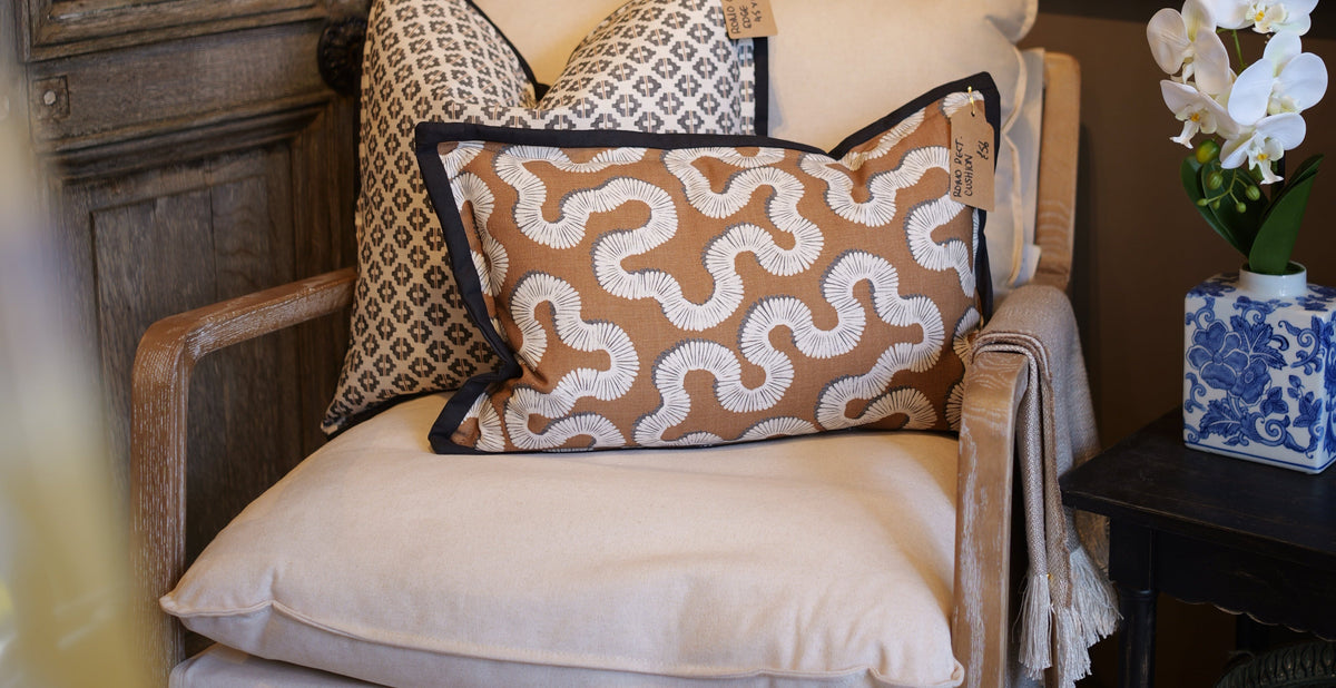 Decorative cushions on a chair with a side table and vase in the background