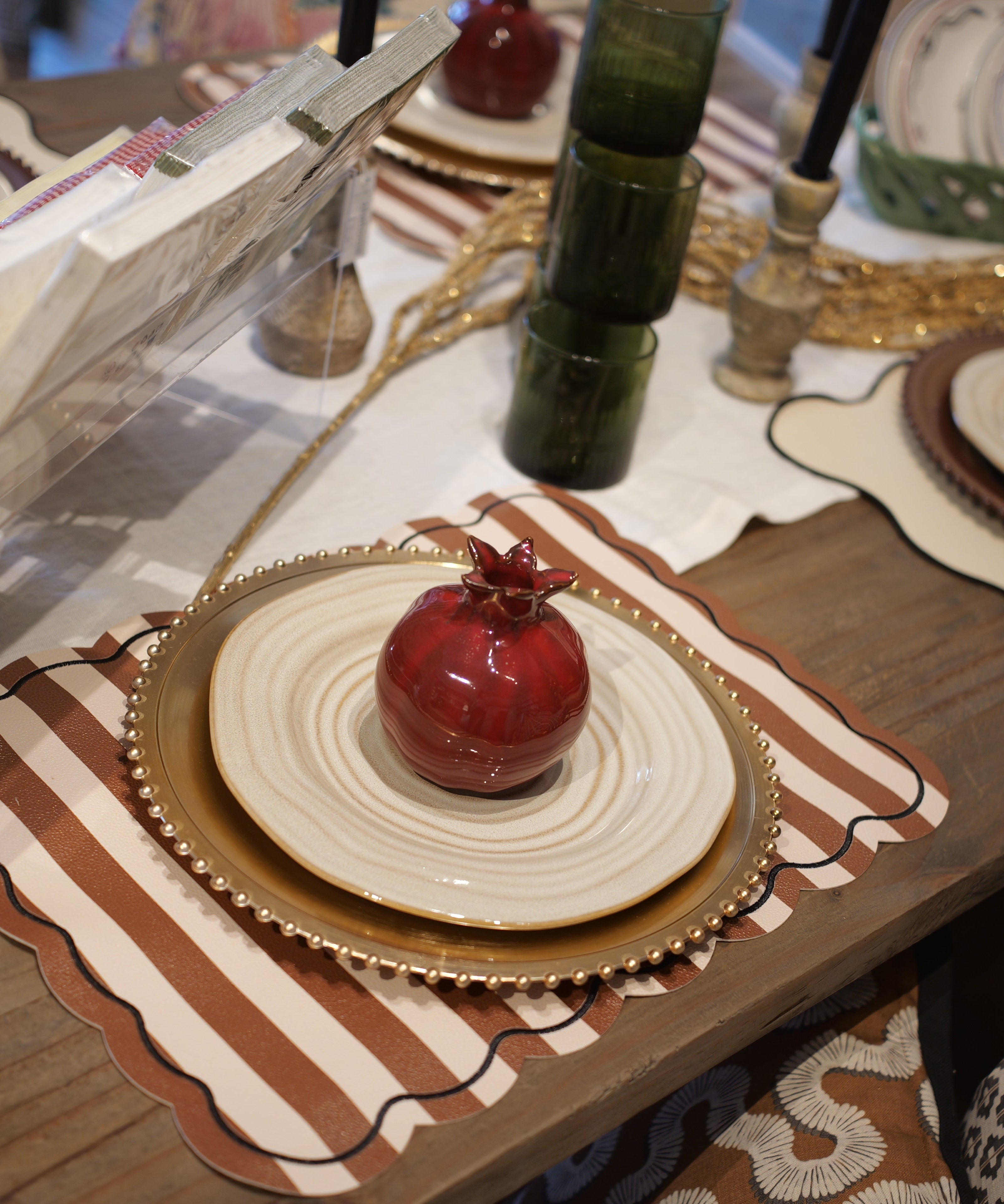 Decorative table setting with pomegranates, plates, and a book on a wooden table.