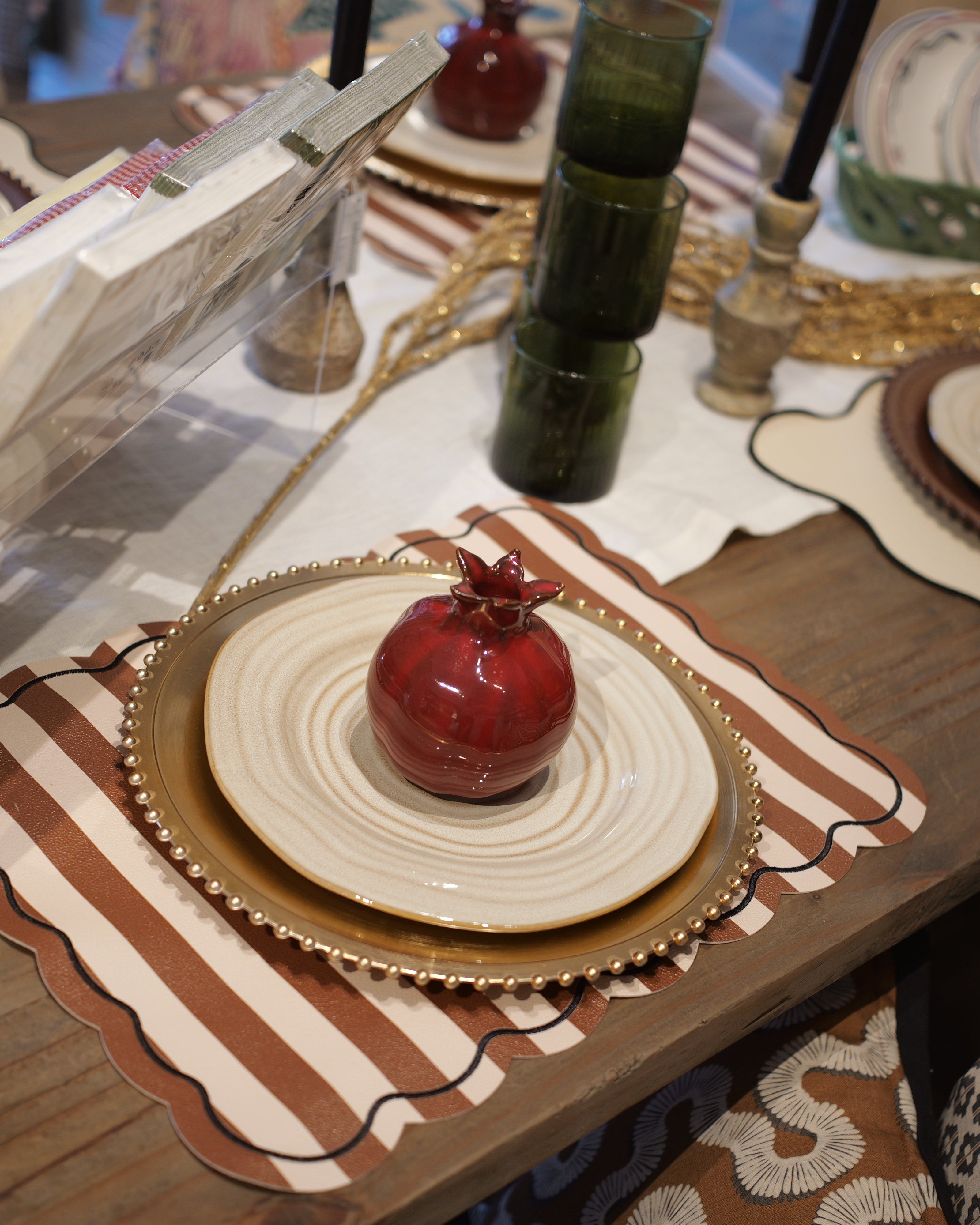 Decorative table setting with pomegranates, plates, and a book on a wooden table.