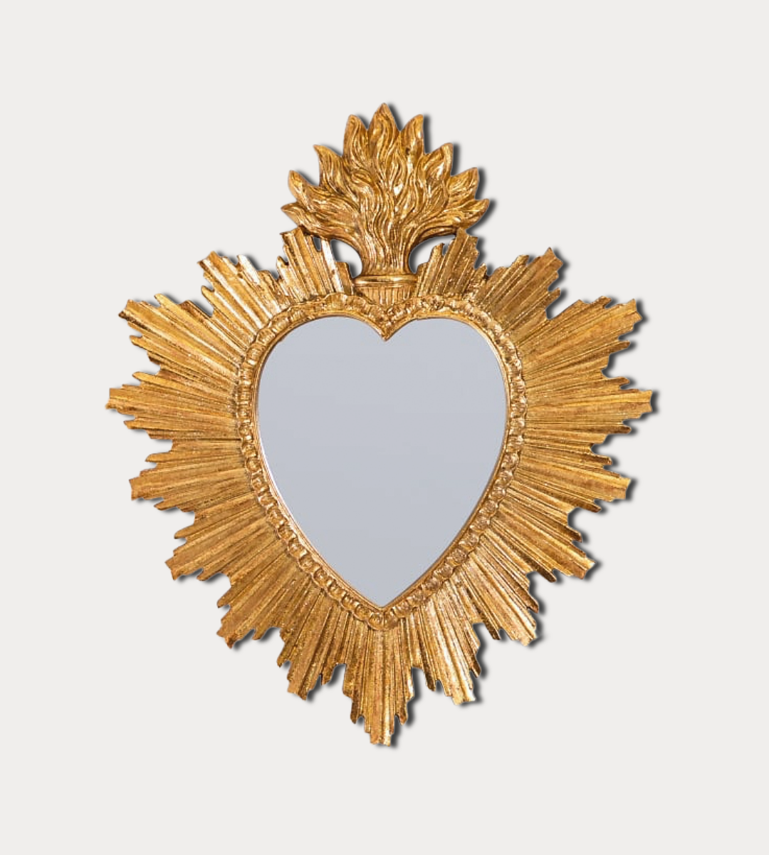 Heart-shaped mirror with gold sunburst frame on a light gray background