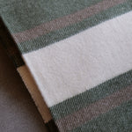 A close-up of a woven textile with a dark green base, a wide off-white stripe, and thin muted pink and brown stripes.