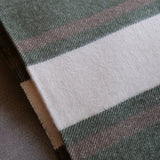 A close-up of a woven textile with a dark green base, a wide off-white stripe, and thin muted pink and brown stripes.