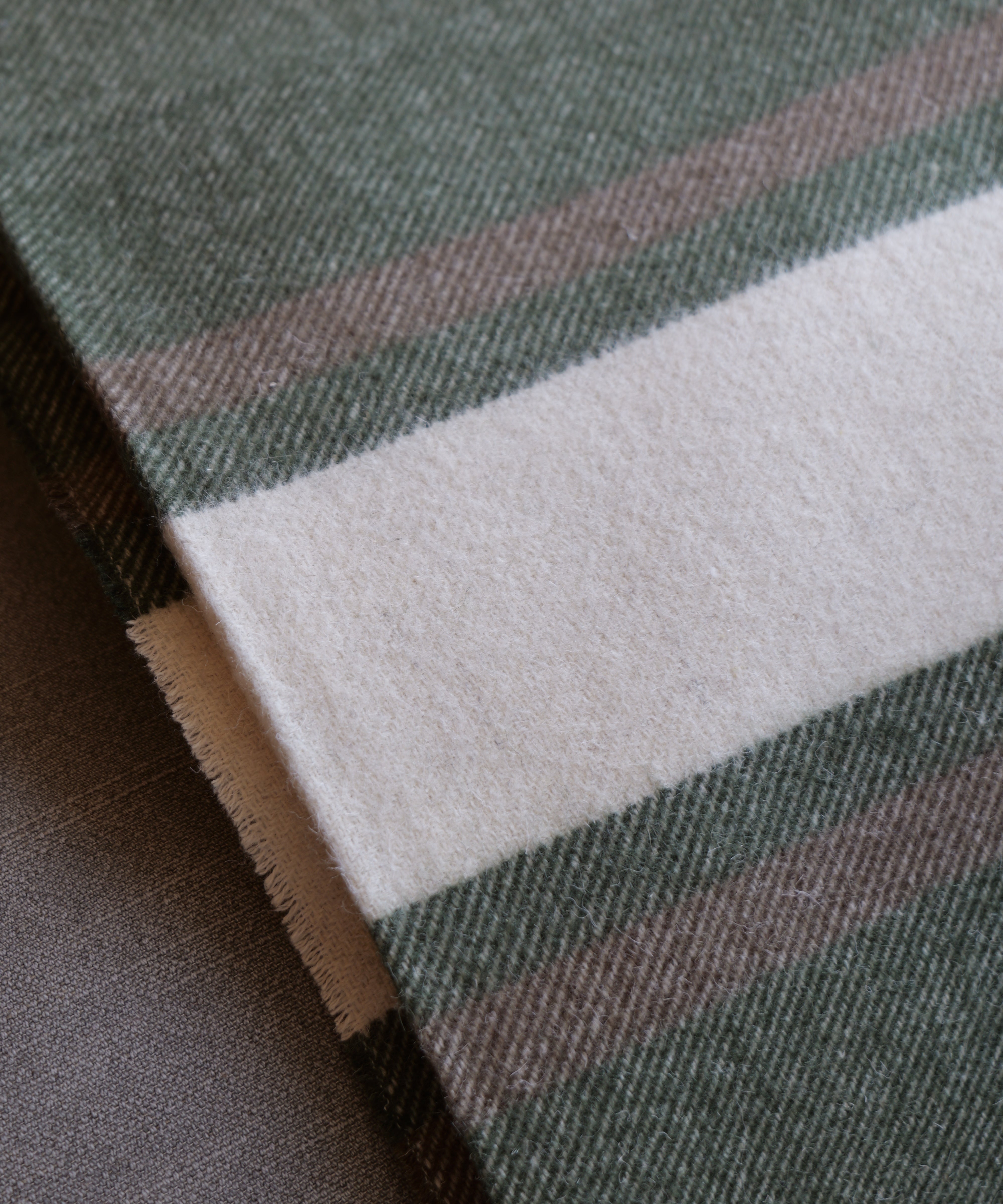 A close-up of a woven textile with a dark green base, a wide off-white stripe, and thin muted pink and brown stripes.