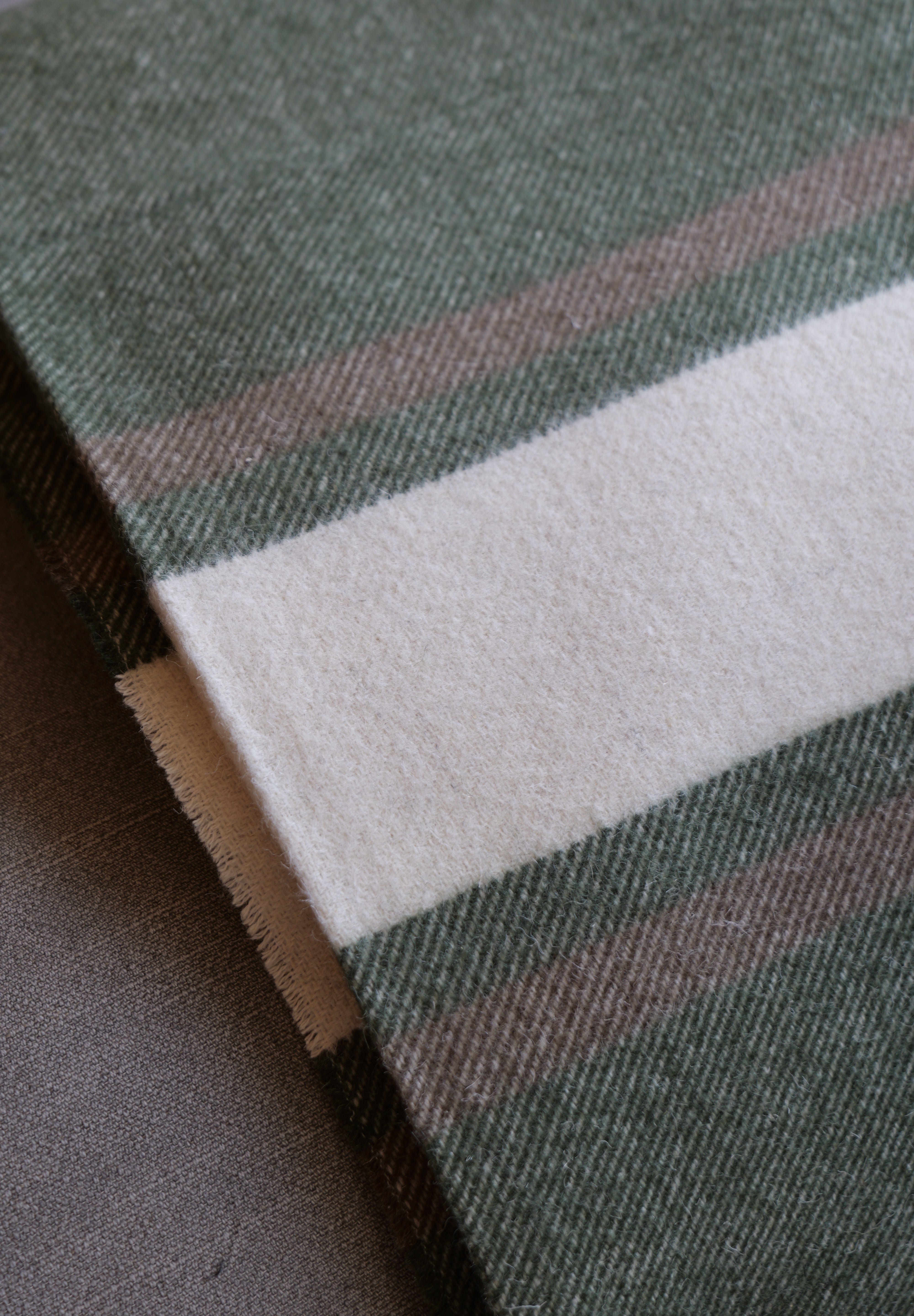 A close-up of a woven textile with a dark green base, a wide off-white stripe, and thin muted pink and brown stripes.