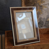 A rectangular picture frame with a layered wood design, featuring a dark brown outer frame, a medium brown inner frame, and a light beige outer border, displayed on a wooden tray in a home setting.