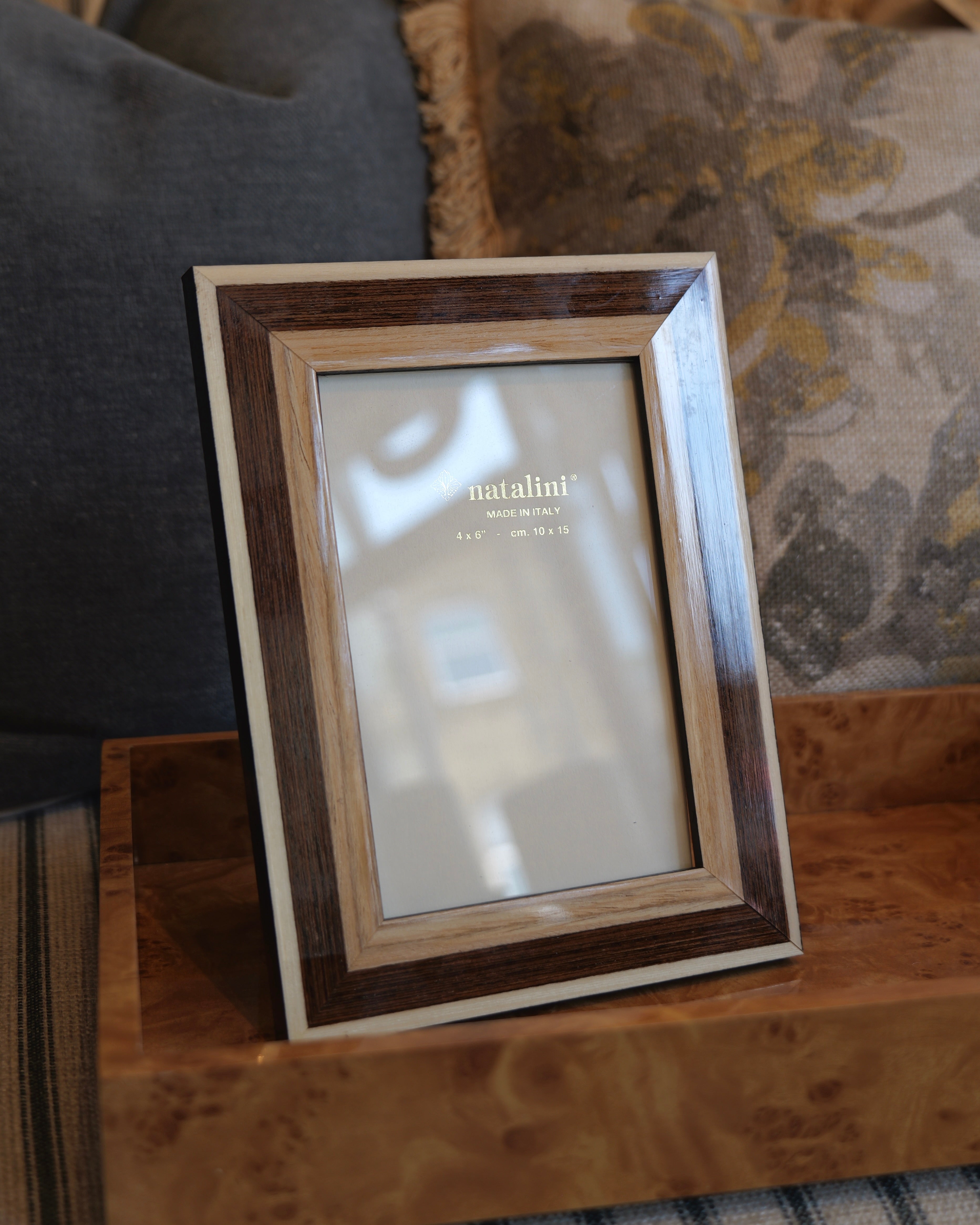 A rectangular picture frame with a layered wood design, featuring a dark brown outer frame, a medium brown inner frame, and a light beige outer border, displayed on a wooden tray in a home setting.
