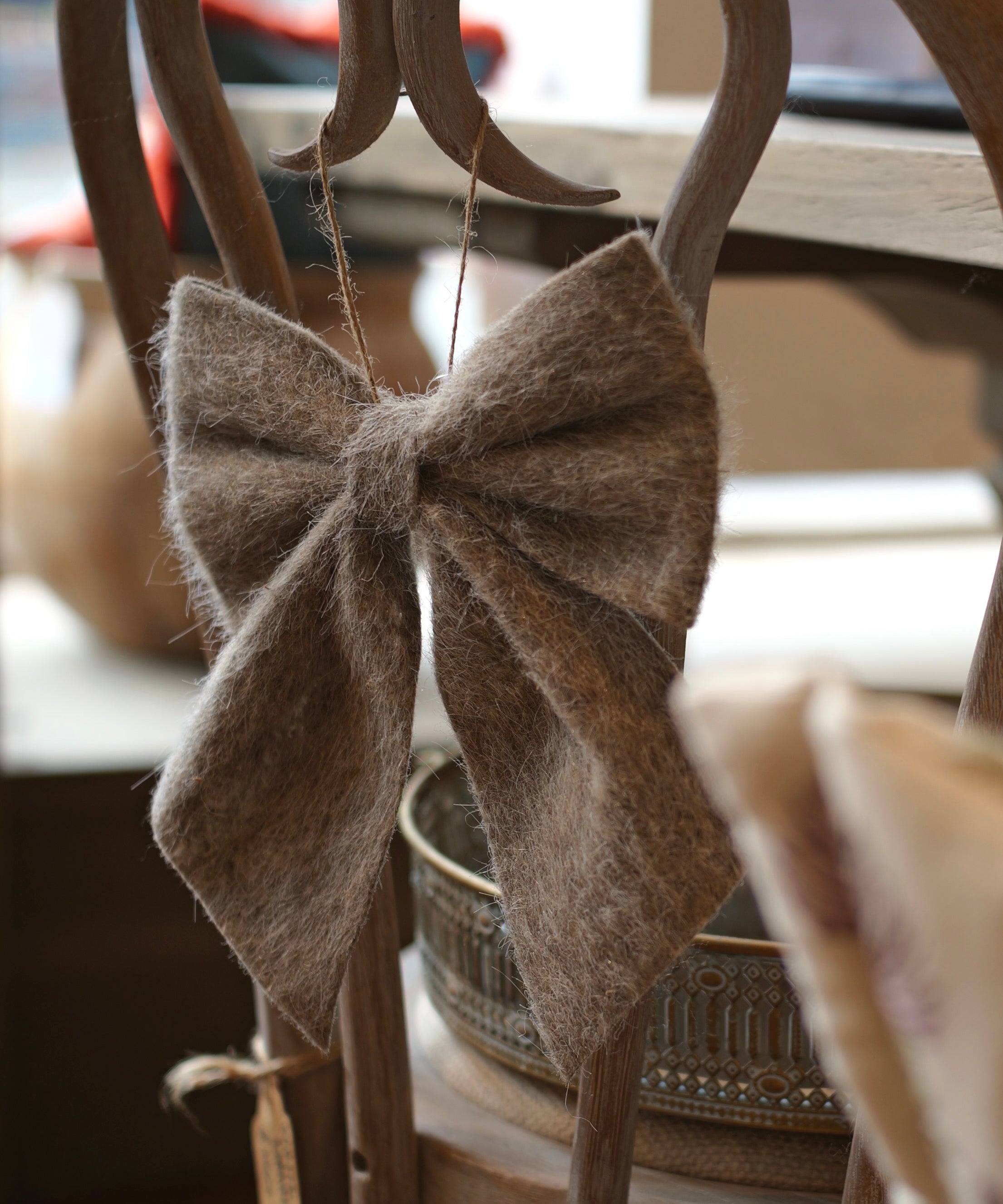 A large, fuzzy brown felt bow hanging from a wooden chair in a softly blurred indoor setting.
