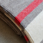 A close-up of folded woven fabric with a heather gray base and bold red and off-white stripes.