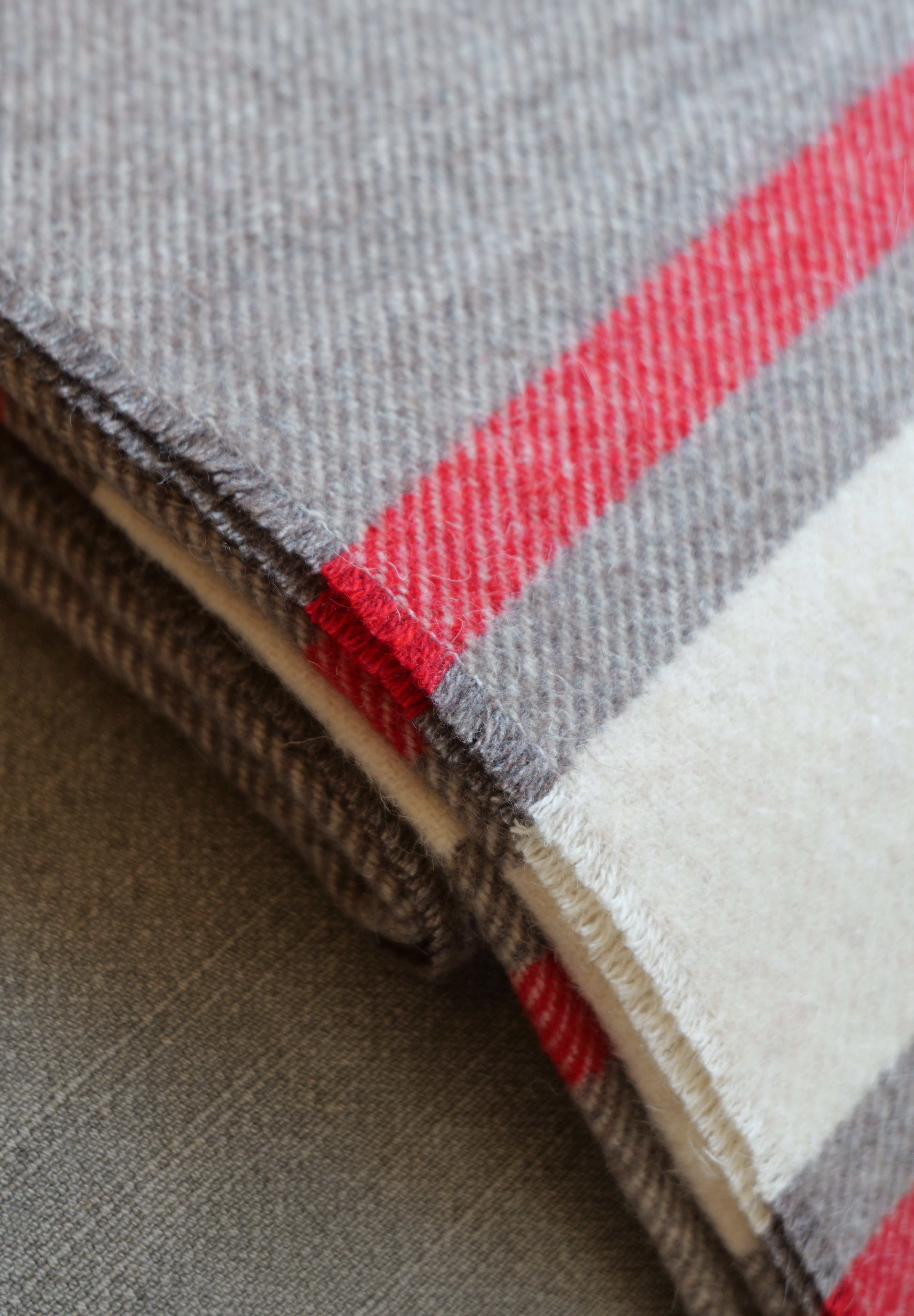 A close-up of folded woven fabric with a heather gray base and bold red and off-white stripes.