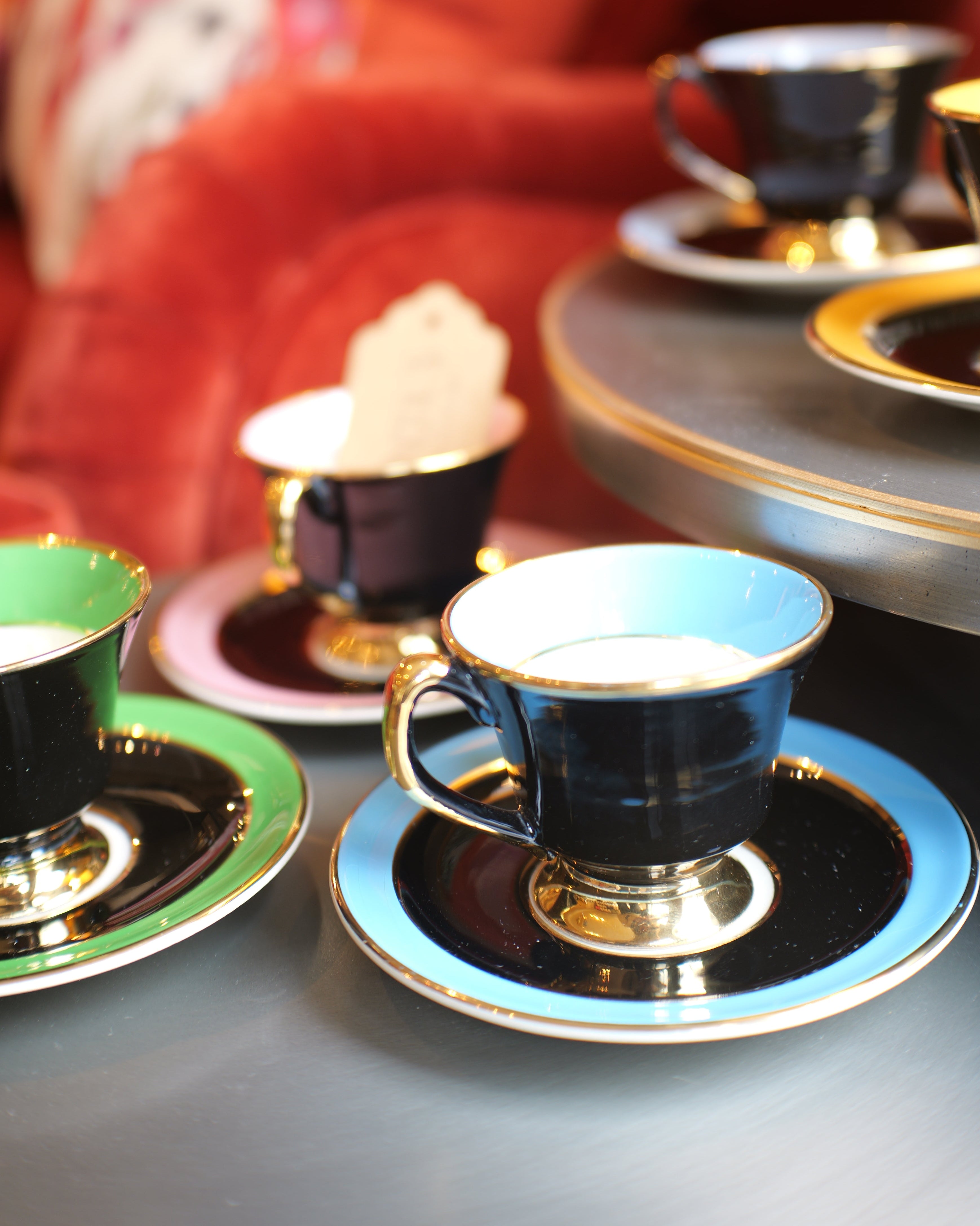 Teacups and saucers on a table with a red cushioned chair in the background