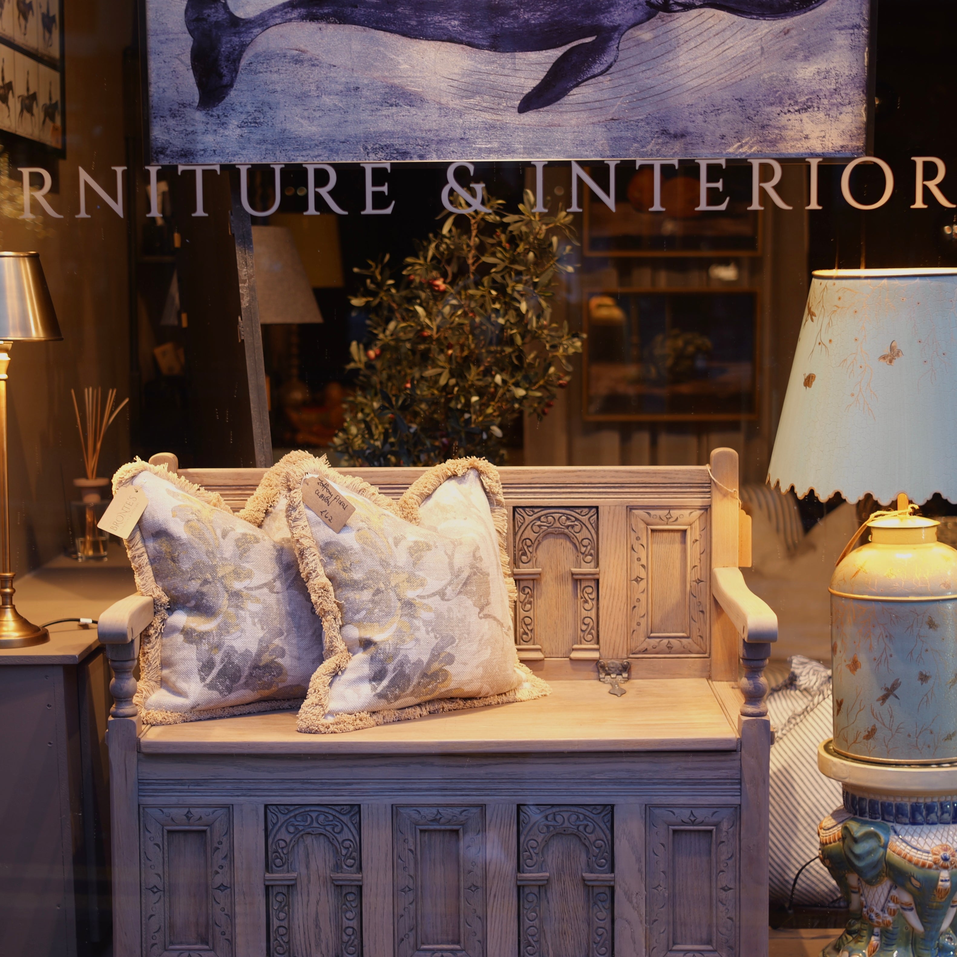 Decorative bench with ornate carvings and pillows in a room setting with a whale painting on the wall.
