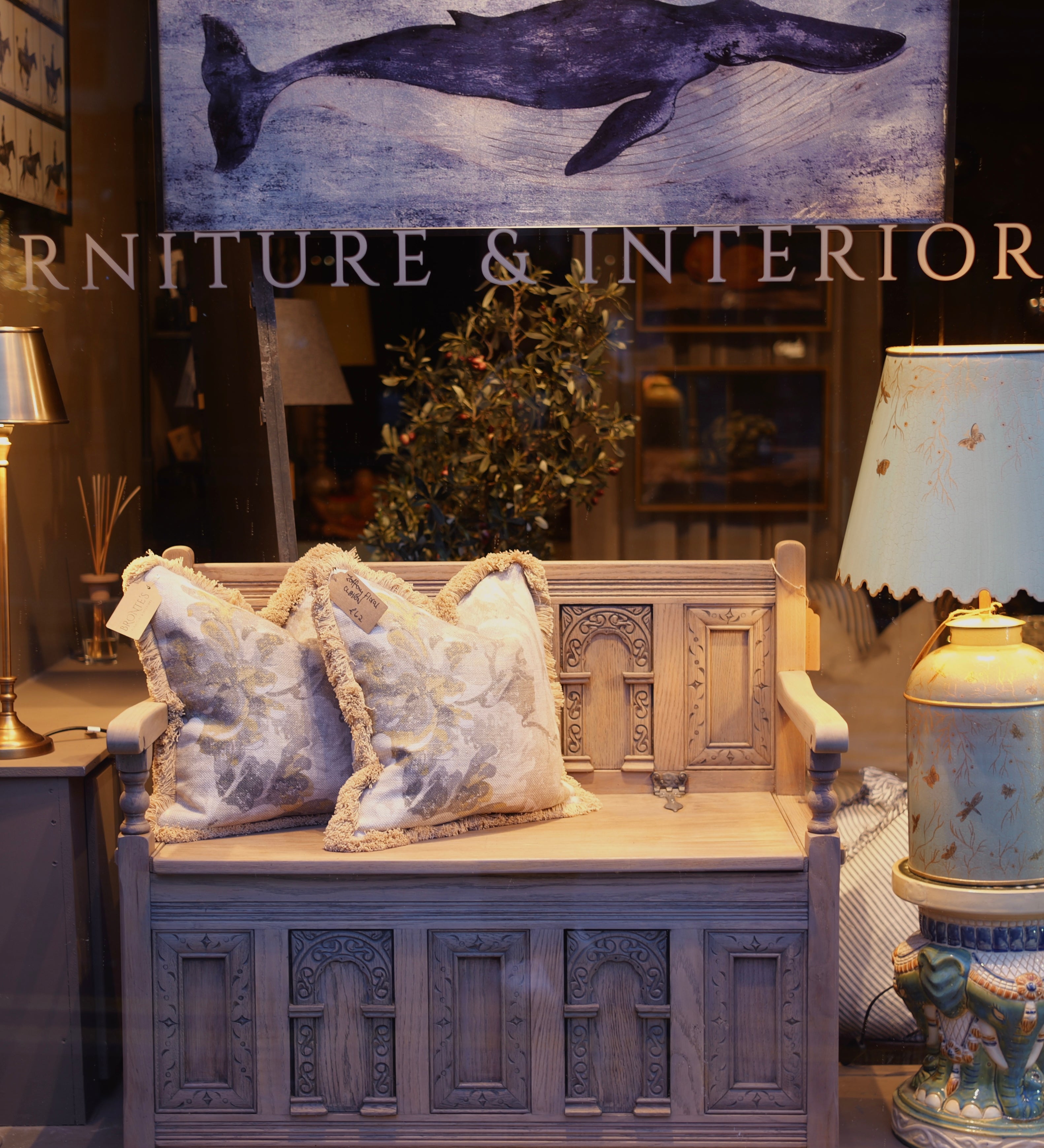Decorative bench with ornate carvings and pillows in a room setting with a whale painting on the wall.