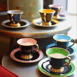 Colorful teacups and saucers on a table with a decorative canister in the background.