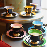 Colorful teacups and saucers on a table with a decorative canister in the background.