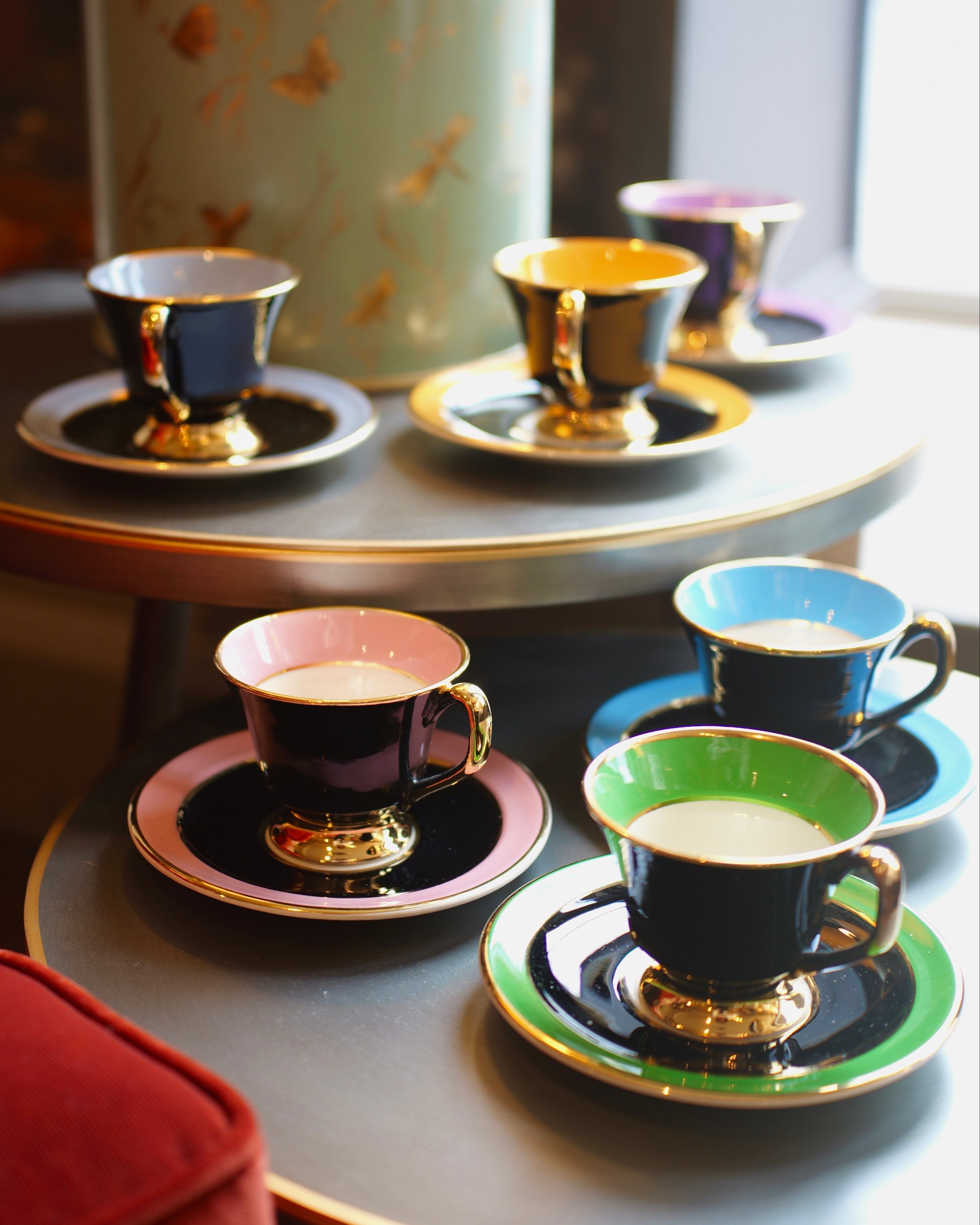 Colorful teacups and saucers on a table with a decorative canister in the background.